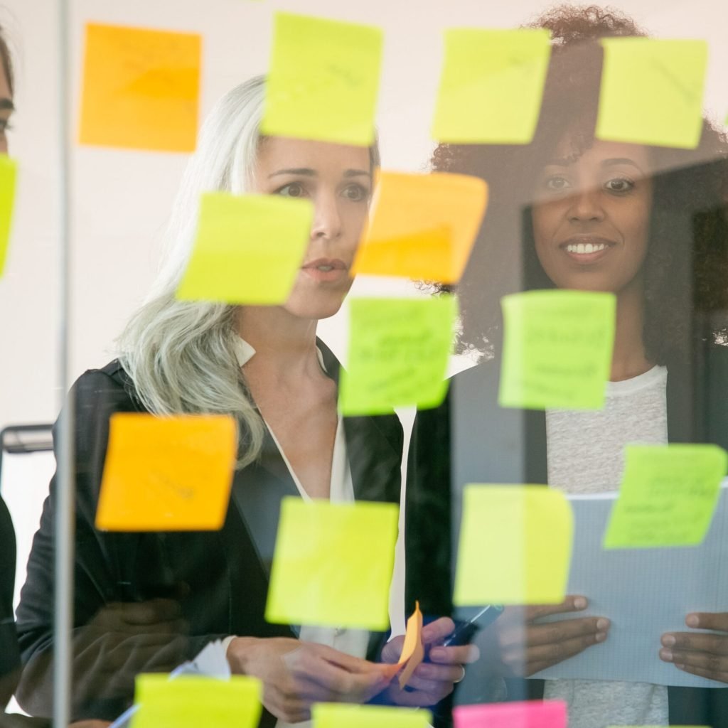 Content young businesspeople discussing marketing plan and making notes on stickers. Successful confident colleagues in suits meeting in office room. Teamwork, business and brainstorm concept